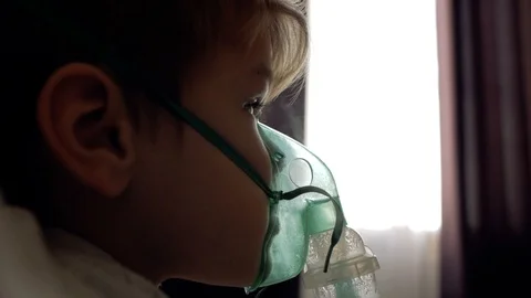 The boy makes inhalation at home on the bed opposite the window Stock Footage 103697206