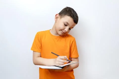 The boy makes notes in a notebook with a pencil. Stock Photos