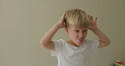 A boy is making funny faces at the camera, holding both hands to his ears and Video stock 322203211