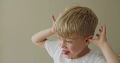A boy is making funny faces at the camera, holding both hands to his ears and Stock Footage 324825769