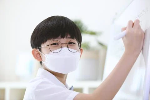 A boy in a mask smiling brightly while solving problems in front of a blackboard 写真素材