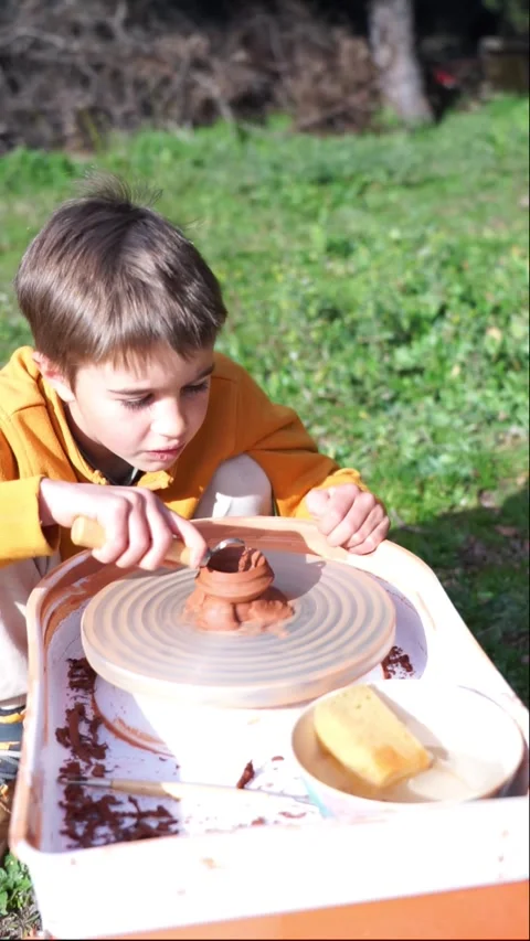 Boy molding clay with a pottery tool on an outdoor potter's wheel Stock Footage 263757461