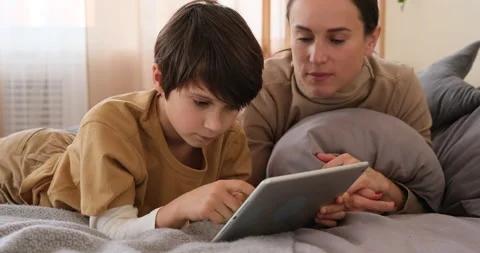 Boy with mother lying on bed and playing on digital tablet Stock Footage 145236523