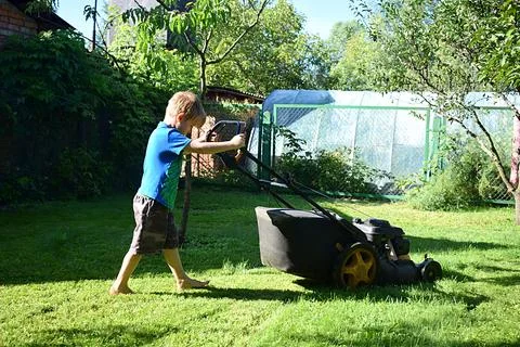 The boy mows the lawn with a mower 写真素材
