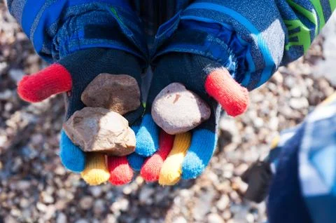 A boy in multi-colored gloves holds stones. Stock Photos