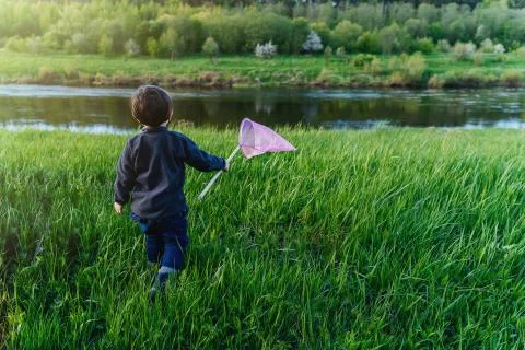 A boy with a net walks on the grass to the river Stock Photos
