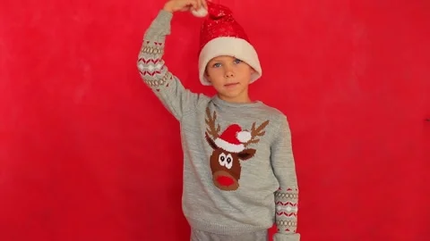 Boy in a New Year's cap and sweater on a red background. Video stock 160953840