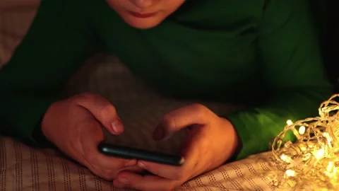 A boy at night in the dark lying on the bed holds a smartphone in his hands Stock Footage 165395593