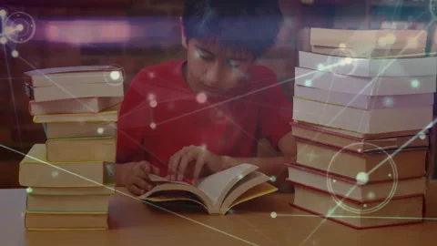 Boy opening book on table and activating floating digital graphics while reading Stock Footage 312280313