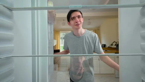 Boy opening empty fridge, looking inside and smiling while searching for food Stock Footage 309393446