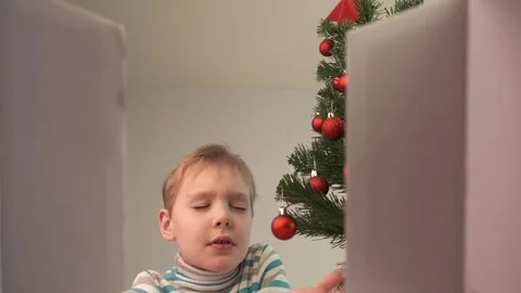 Boy opening the gift box near the christmas tree. Holidays concept. Video stock 166385678