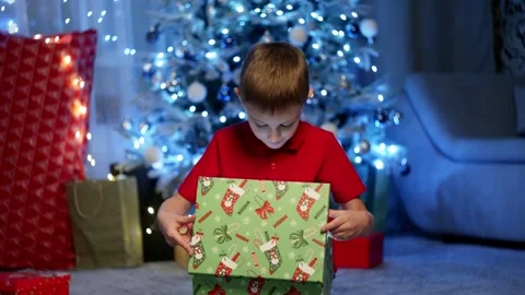 A boy opens a gift from Santa under the Christmas tree. Stock Footage 258358744