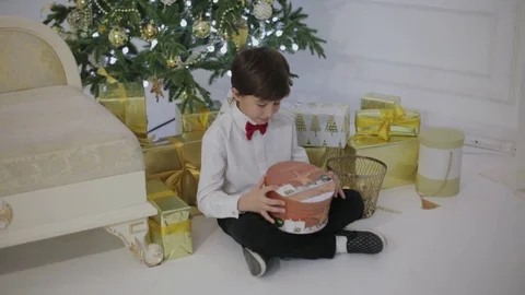 Boy opens New Year's gift sitting under the decorated Christmas tree Stock Footage 83300684