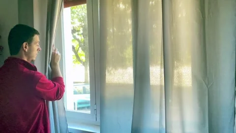Boy opens the window curtain at home to look outside Stock Footage 255445050