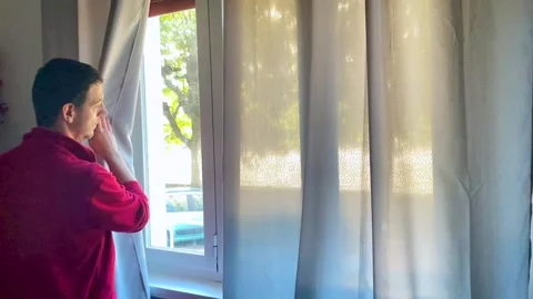 Boy opens the window curtain at home to look outside Stock Footage 255445063