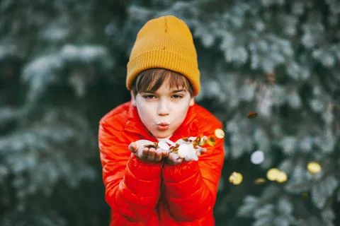 A boy in an orange jacket and hat holds shiny confetti in his hands and blows on Stock Photos