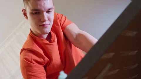 Boy in Orange Shirt Cleaning Table with Focused Expression Stock Footage 319917041