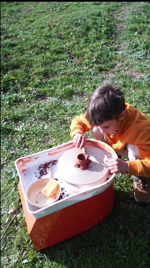Boy outdoors making pottery on a potter's wheel Stock Footage 263757465