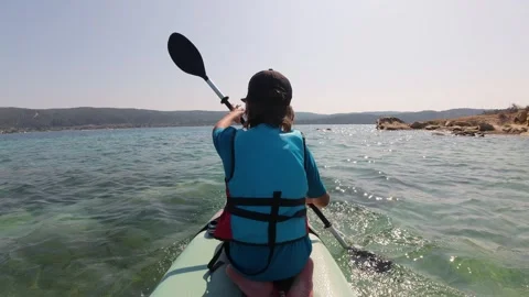 Boy paddling on a stand up paddleboard while sitting. Rear view of child in life Stock Footage 313808776