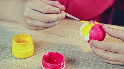 A boy painting an Easter egg with red paintbrush on a wooden table. Stock Footage 172220522