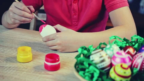 A boy painting an Easter egg with red paintbrush on a wooden table Stock Footage 172220524