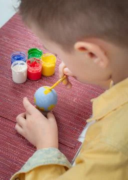 A boy painting an Easter egg on a red fabric background. Painting Easter eggs Foto stock