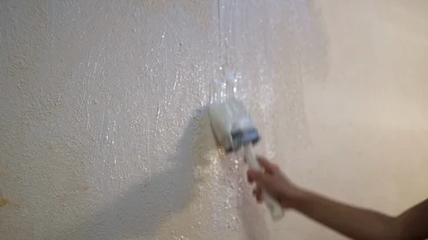 Boy paints a wall with white paint with a brush. Video picture. Shot from behind Vídeos de archivo 119978359
