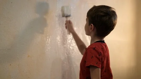 Boy paints a wall with white paint with a brush. Video picture. Shot from behind Stockbeeldmateriaal 119979883