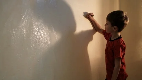 Boy paints a wall with white paint with a brush. Video picture. Shot from behind 스톡 동영상 119980281