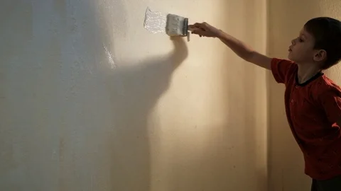 Boy paints a wall with white paint with a brush. Video picture. Shot from behind 스톡 동영상 119981337