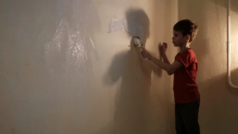 Boy paints a wall with white paint with a brush. Video picture. Shot from behind Vídeos de archivo 119982267