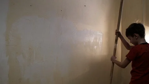 The boy paints the wall with white paint roller. Video picture. Shot from behind 動画素材 119996672