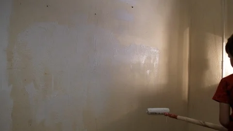 The boy paints the wall with white paint roller. Video picture. Shot from behind 動画素材 119996976