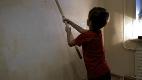 The boy paints the wall with white paint roller. Video picture. Shot from behind Stock Footage 119997474