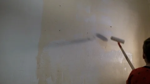 The boy paints the wall with white paint roller. Video picture. Shot from behind Stock Footage 119997679