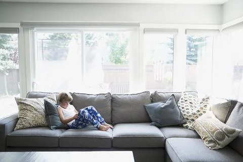 Boy in pajamas using digital tablet on living room sofa Stock Photos