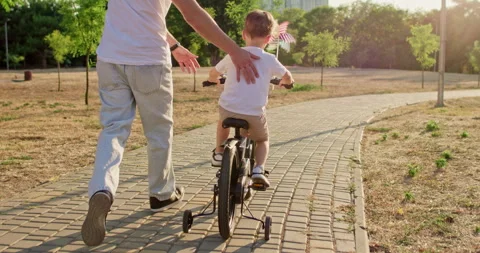 Boy pedals bicycle with pinwheel while father walks behind son Stockbeeldmateriaal 316764684