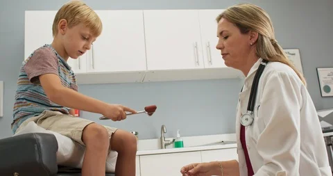 Boy at pediatric office checking his reflexes with hammer while doctor watches Stock-Footage 103029718