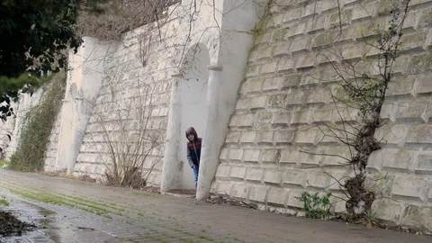 Boy peeks out of white wall and claps his hands,it is raining in tropical park Stock Footage 128243288