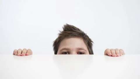 Boy peeps from under the table on a white background Stock Footage 239423737
