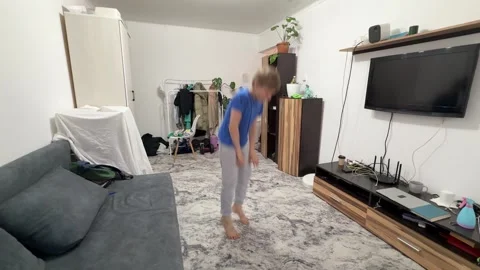 Boy performing squat jump in living room, bending down and jumping upward during Stock Footage 335645794