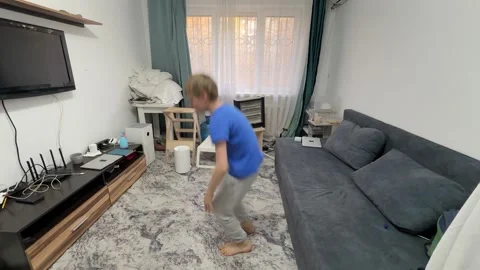Boy performing squat jump in living room, bending down and jumping upward during Stock Footage 336964401
