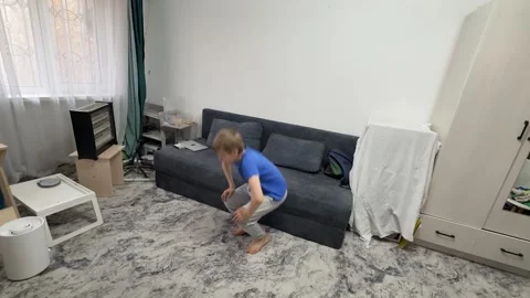 Boy performing squat jump in living room, bending down and jumping upward during Stock Footage 336964456