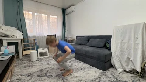 Boy performing squat jump in living room, bending down and jumping upward during Stock Footage 336964461
