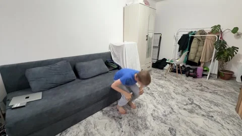 Boy performing squat jump in living room, bending down and jumping upward during Stock Footage 336964470