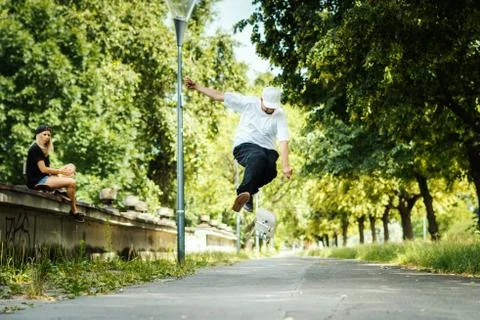 Boy performs a trick on a skateboard while the girl sits and watches Stock Photos