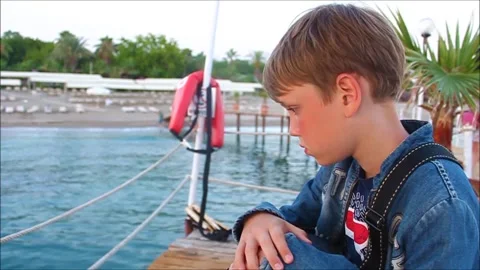 The boy on the pier looks thoughtfully at the water. The concept of vacation Stock Footage 153867014