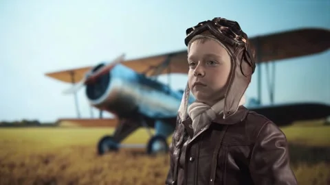 Boy pilot with binoculars standing in field against background of old biplane. Video stock 309958632