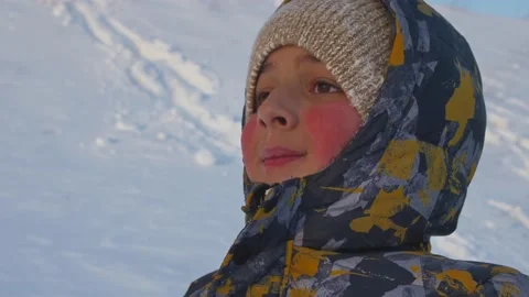 A boy with pink cheeks in a hat and jacket smiles against a background of snow. Stock Footage 150567221