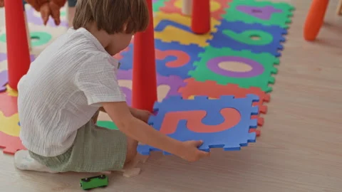 Boy placing a blue foam puzzle tile with right hand on a colorful number pl.. Stock Footage 339204690